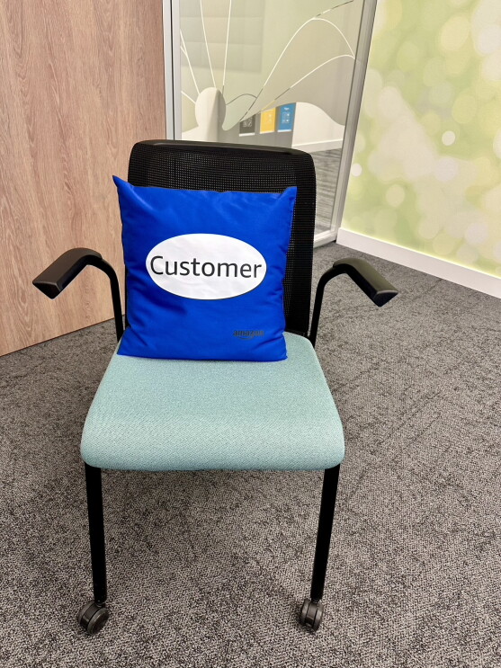 Ein schwarz-grüner Konferenzstuhl bei Amazon, auf dem ein blaues Kissen mit der Aufschrift Customer liegt.