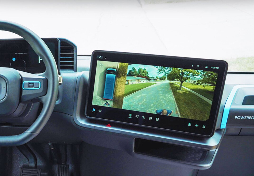 A photo of the screen within a dashboard of an Amazon delivery van from Rivian. The screen is displaying the view from the 360-degree camera, of both a bird's-eye-view of the van, and the rear of the van.