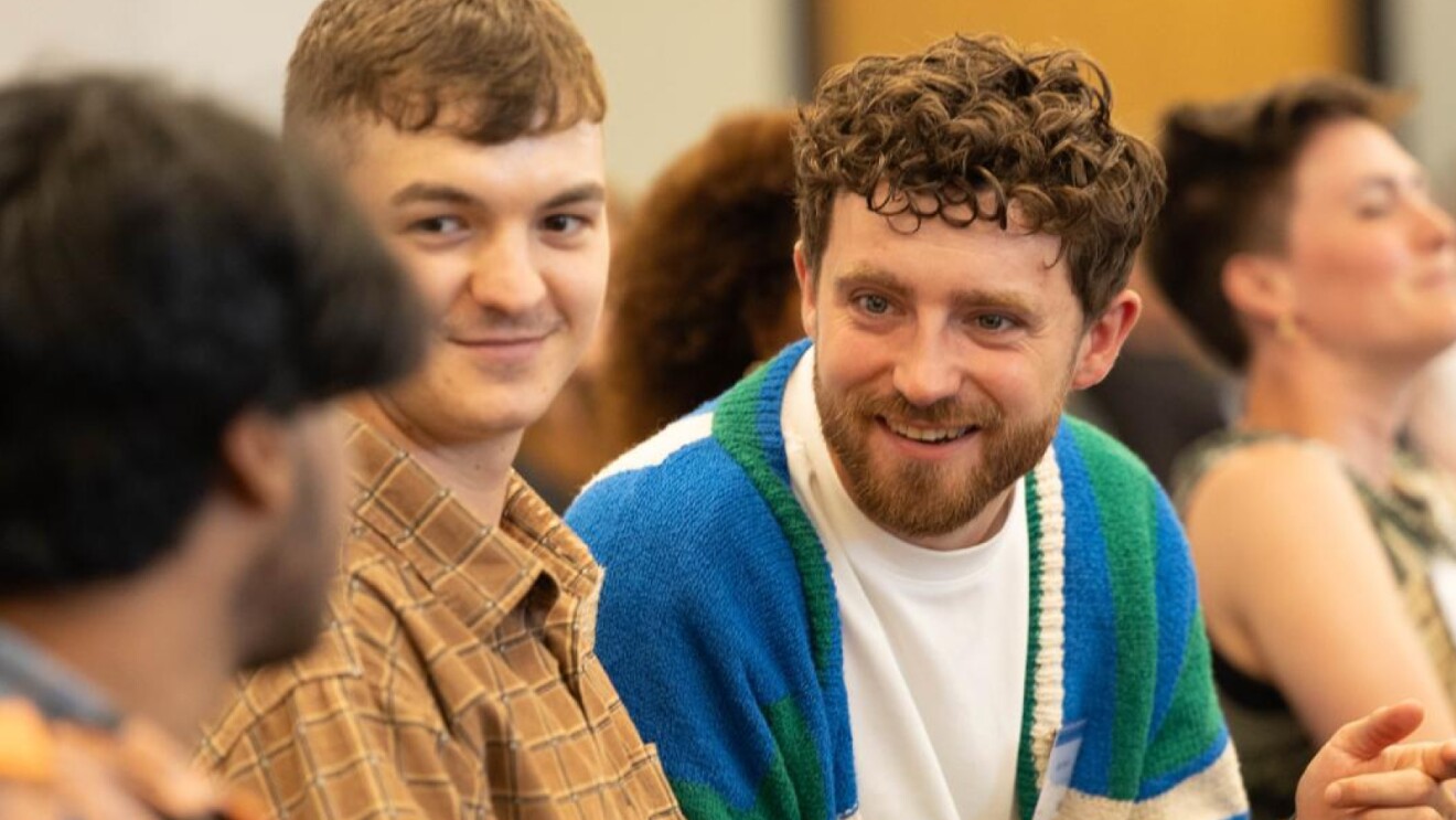 Two smiling young men at social gathering, one in plaid shirt, other in blue sweater