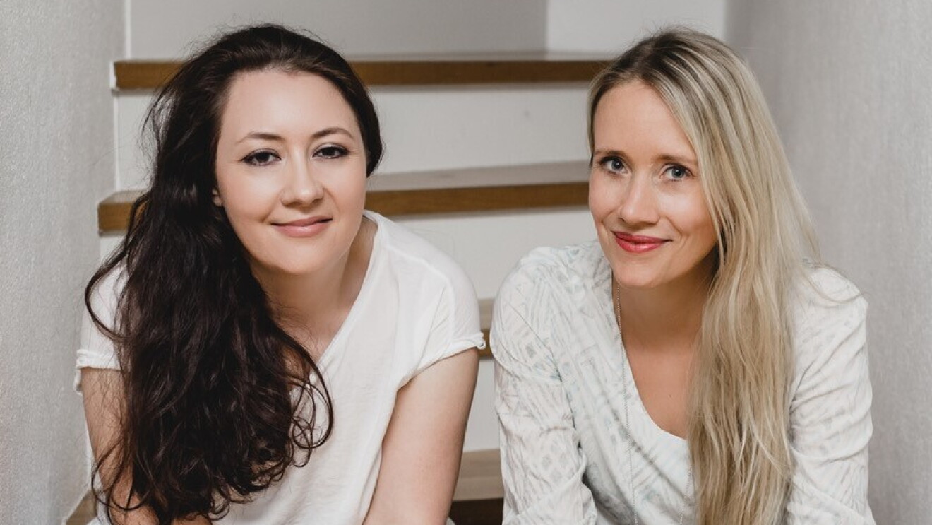 Gruppenfoto des Fantasy-Autorenduos „Rose Snow“, bestehend aus Carmen Schmit und Ulrike Mayrhofer, die beide auf einer Treppe sitzen.
