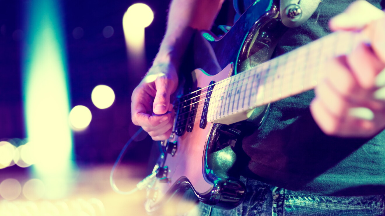 Close-up image of a man playing an electric guitar, with lights blurred out in the background.