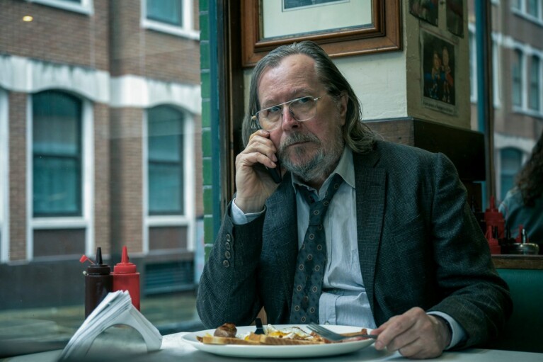 Gary Oldman on the phone whilst eating a cooked breakfast in a café