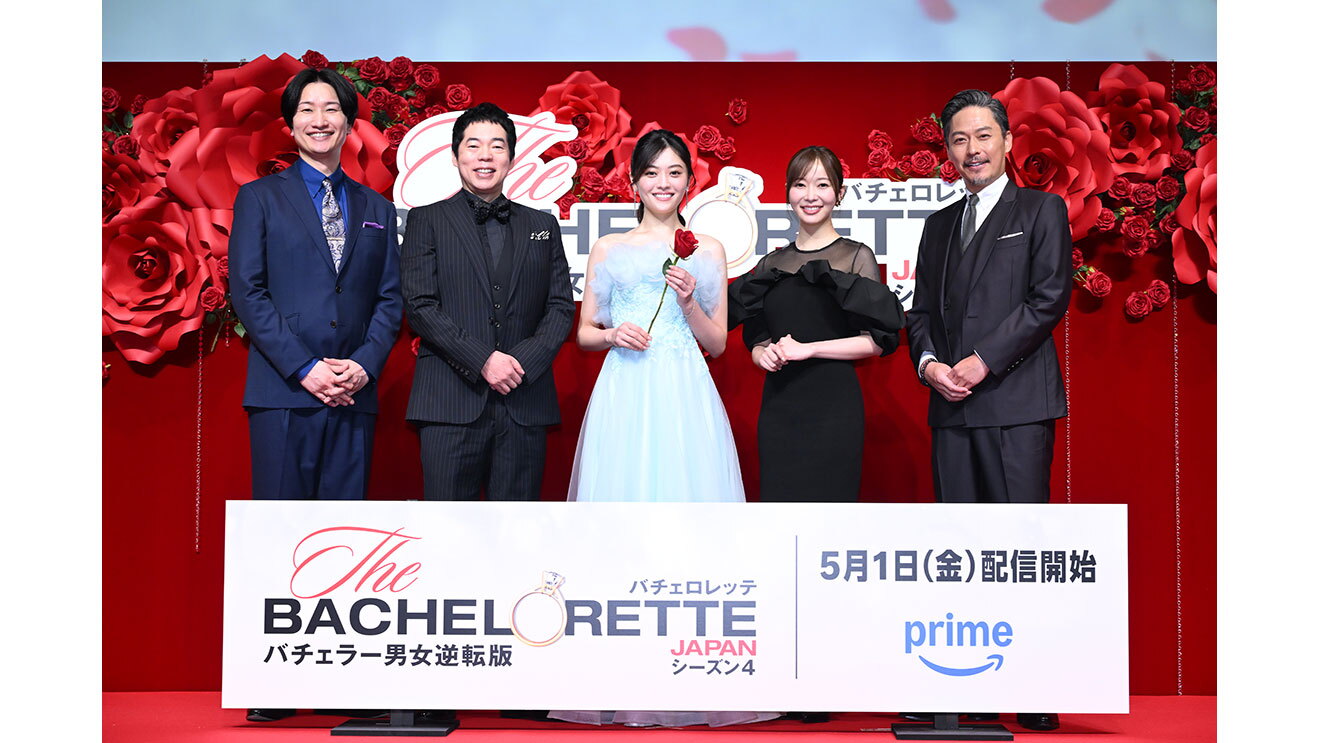 赤いバラの花の大きなオブジェと生花の赤いバラが飾られた赤い壁を背に立つ5人の人物。脚元のパネルに「バチェロレッテ」「バチェラー男女逆転版」と書かれている。