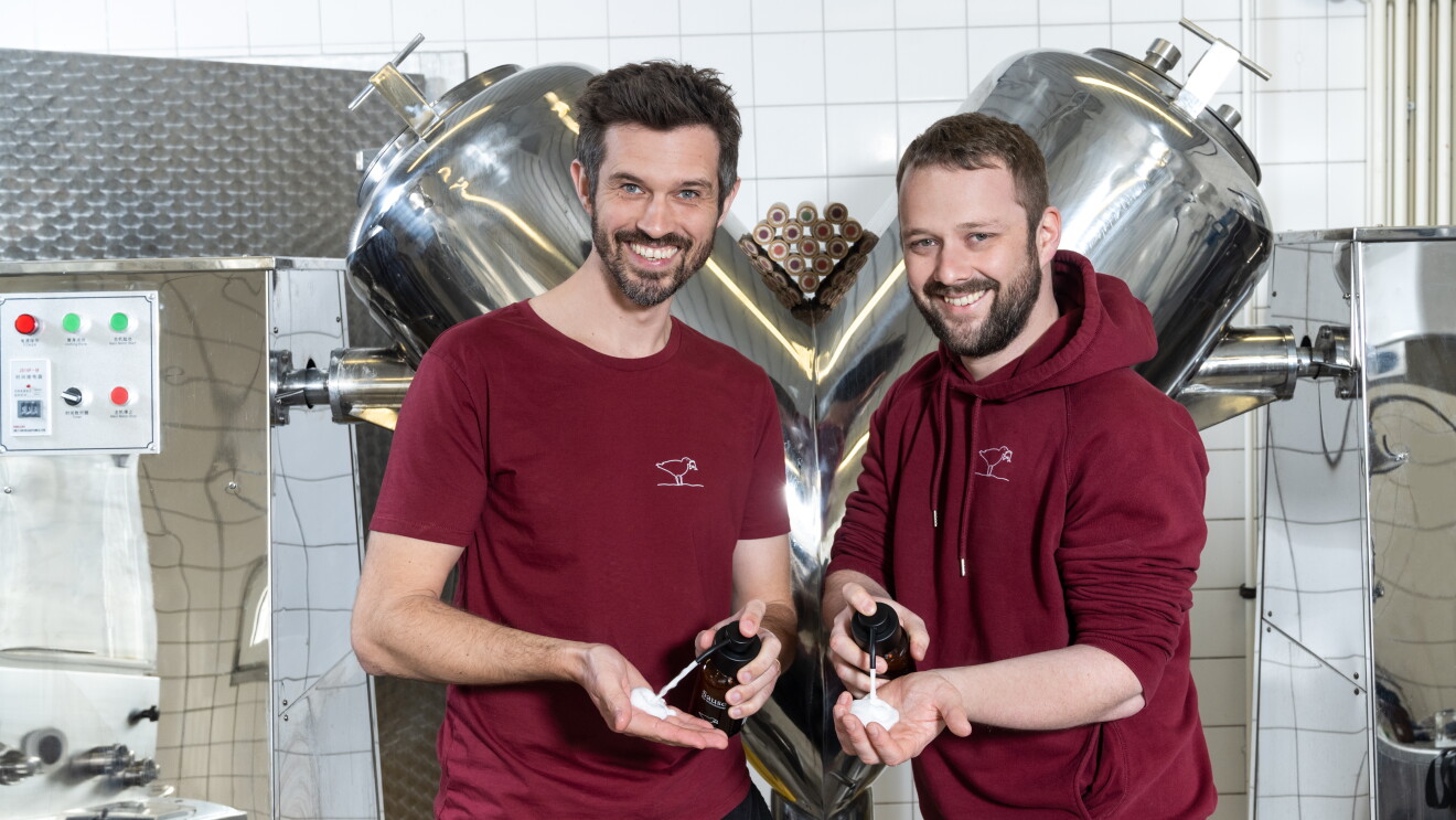 Zwei Männer mit dunklen Haaren und Bart in roten T-shirts haben Seife von Seifenbrause in den Händen und lachen in die Kamera.