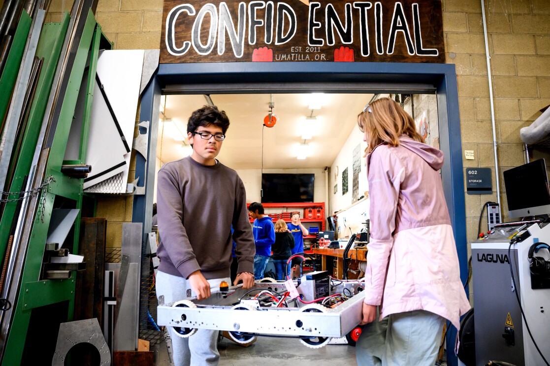 A photo of two students carrying a robot in a classroom.