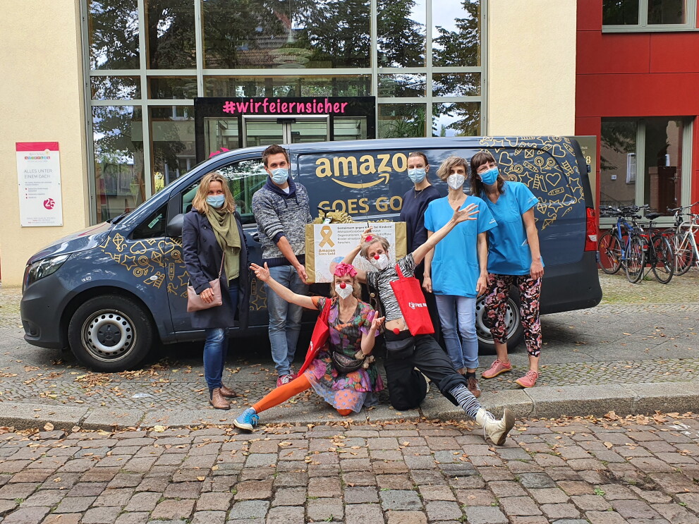 Amazon Mitarbeiter:innen, Rote Nasen Clowns und Krankenhaus Mitarbeiter:innen vor dem mit "Amazon goes gold" beschrifteten Liefervan