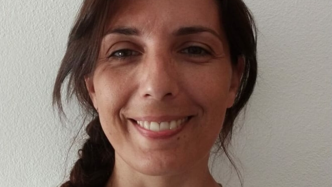 Primo piano della volontaria Amazon Sara. La donna indossa una maglia bianca con un disegno nero, ha i capelli lunghi raccolti in una treccia. 
