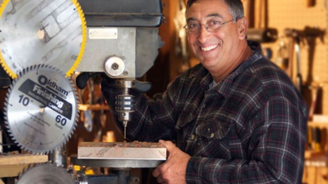 A man stands next to an electric saw and smiles at the camera