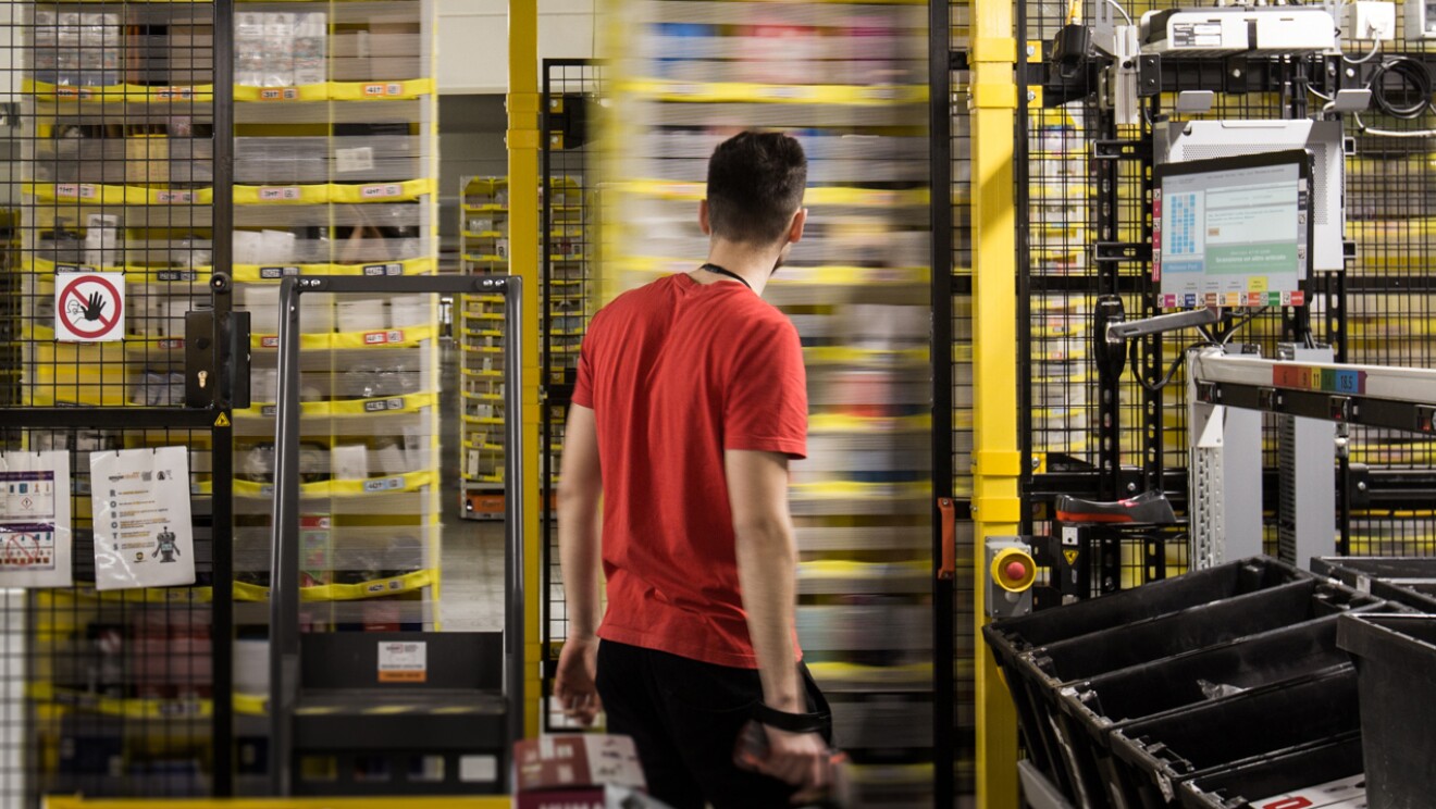 amazon employee in red t-shirt standing infront of moving shelves