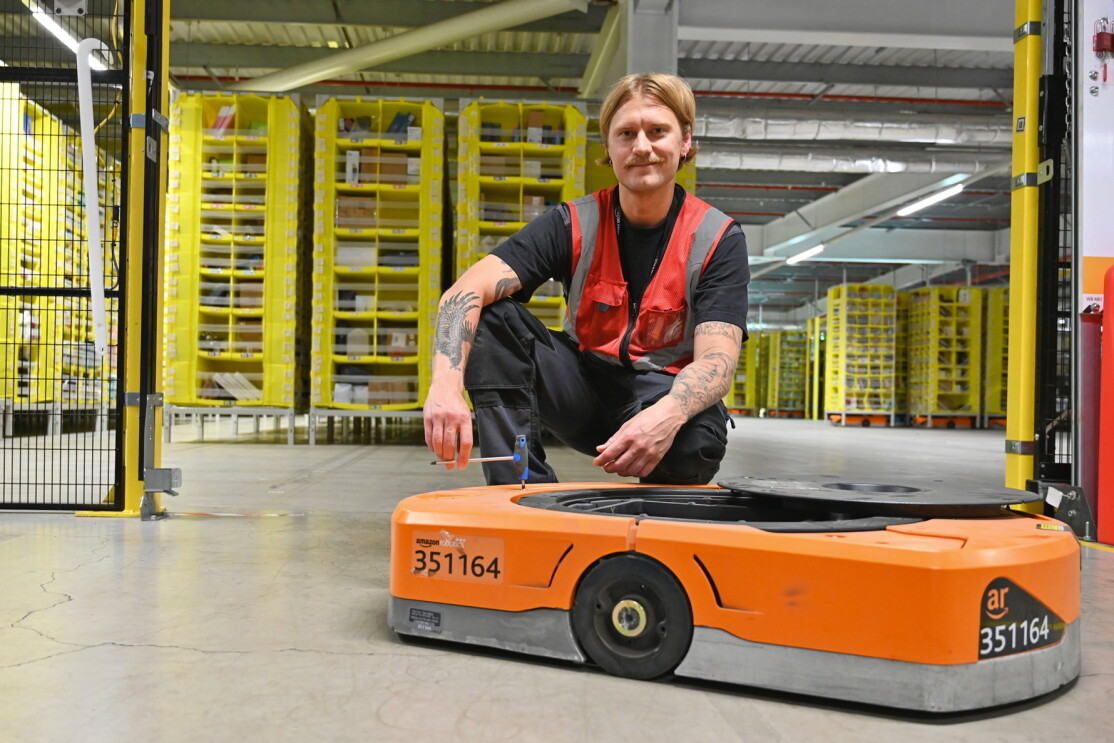 A man kneels next to an Amazon robot 