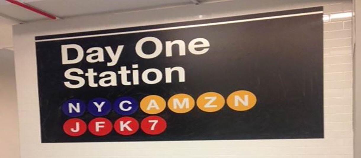 An image of a NYC subway station sign that says "Day One Station, NYC AMZN JFK7" 