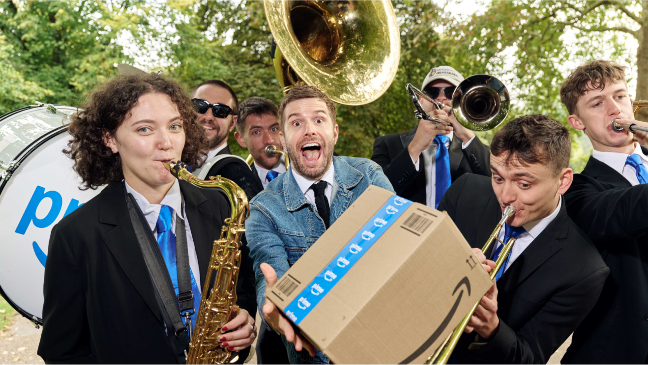 A man holding an Amazon cardboard box while surrounded by a brass band