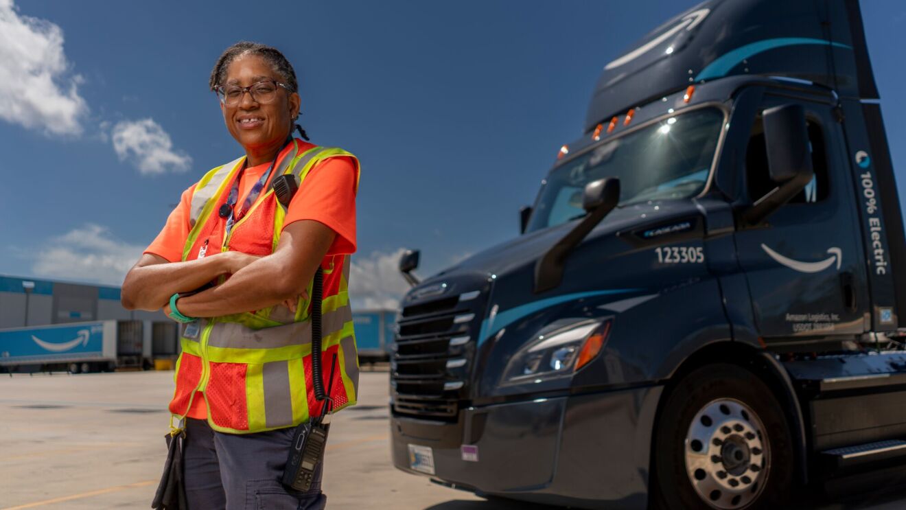 Woman with Amazon driver vest standing next to Amazon delivery truck.