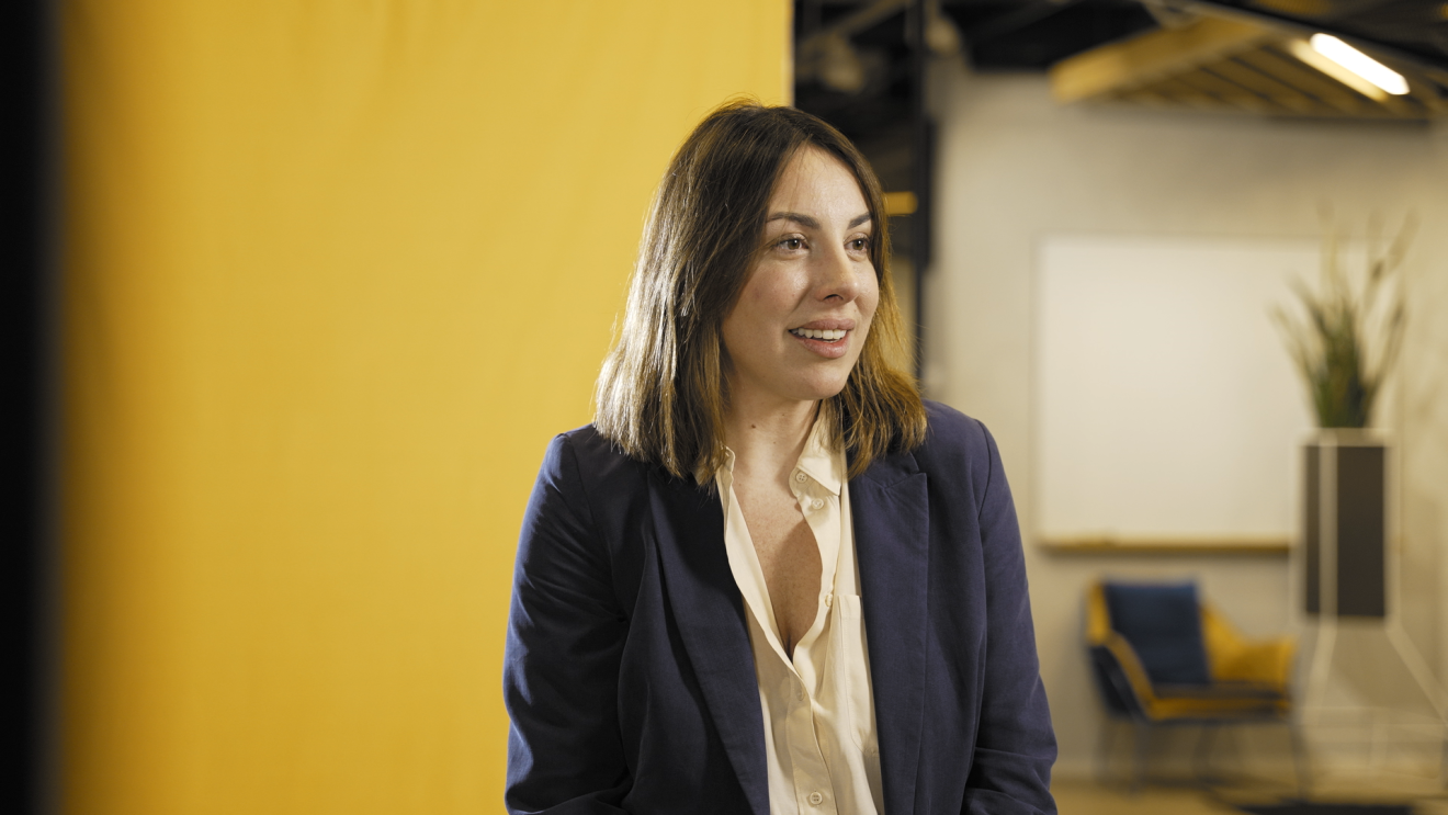 A young woman with a blue jacket and a white shirt is smiling while she explains her job description