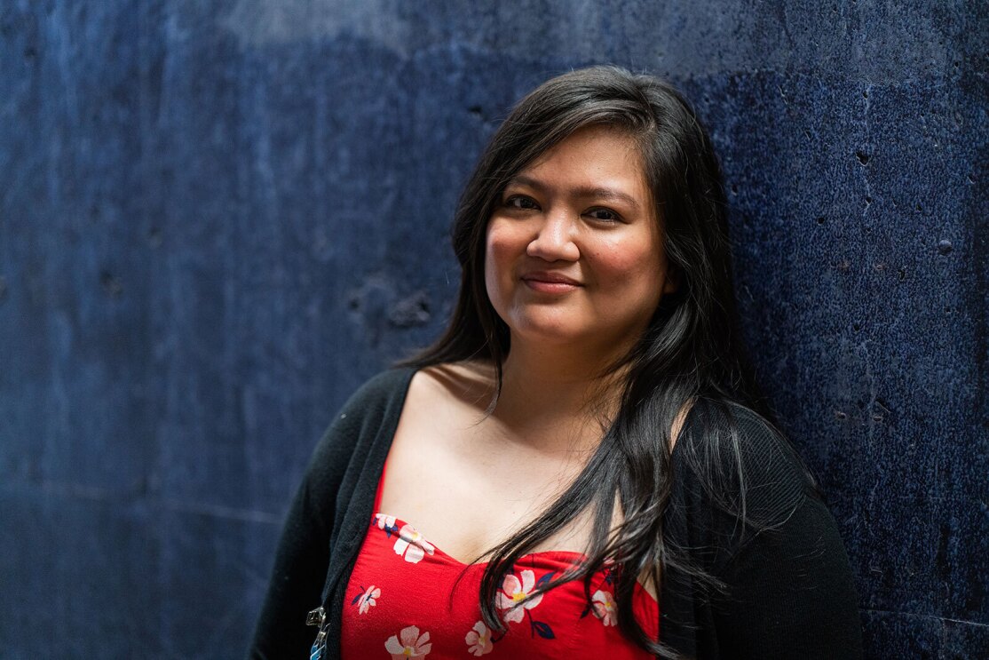 A headshot image of a woman smiling for a photo in front of a dark blue wall.