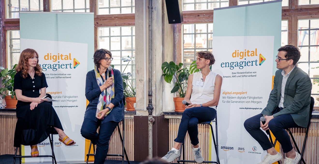 Moderatorin Teresa Sickert, Andrea Frank (Stifterverband), Melanie Stilz (TU Berlin) und Benjamin Brake (Bundesministerium für Digitales und Verkehr) (v.l.) sitzen auf der Bühne der digital.engagiert-Abschluss-veranstaltung und sprechen miteinander.