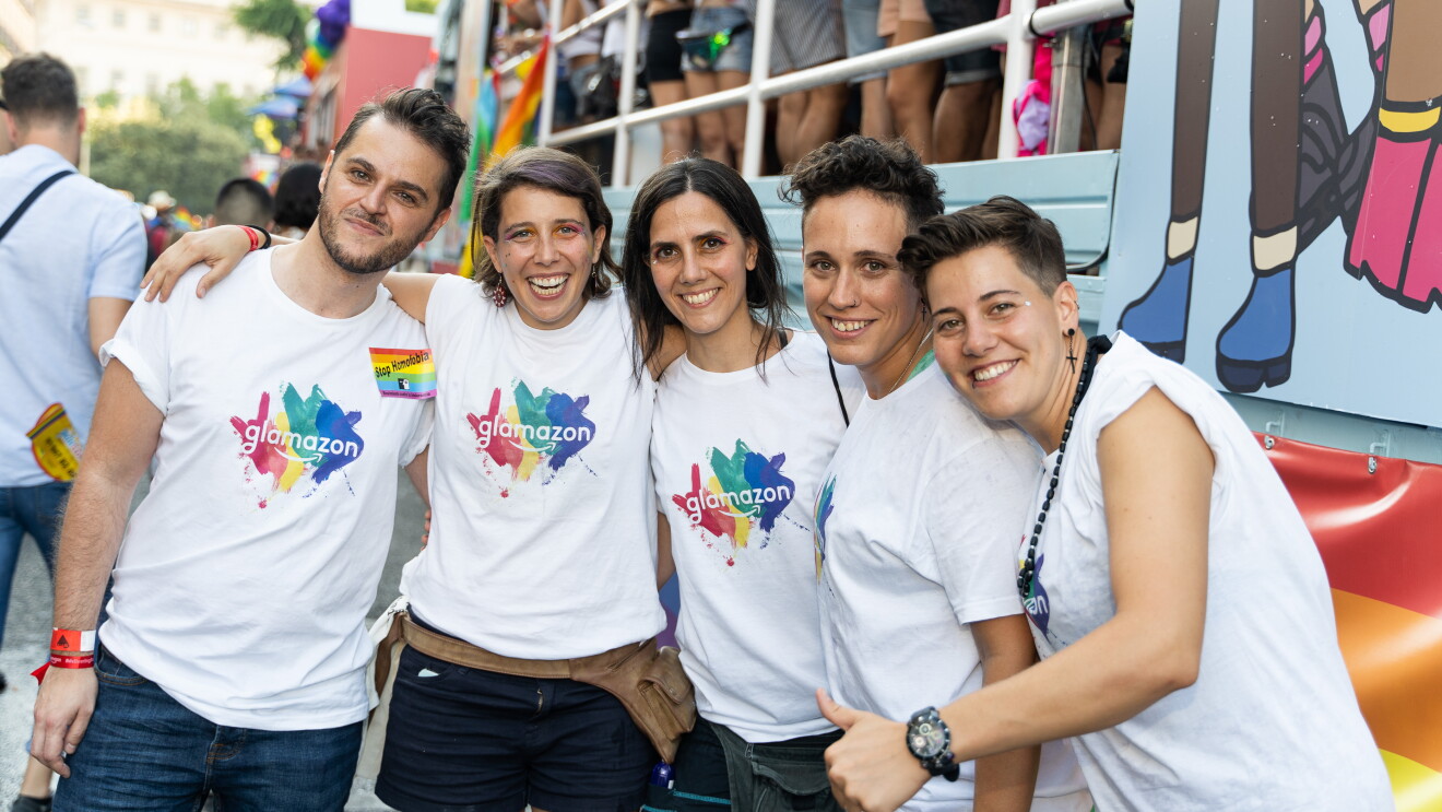 Simone Fortunini, Coia Pons, Eva Ahijado, María García y Susana Torres delante la carroza de glamazon del desfile del Día del orgullo LGTBI. Los cinco lucen la camiseta de glamazon y miran a cámara sonriendo. 