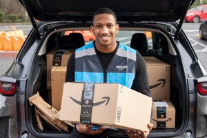 A photo of Quarterback Michael Penix Jr., sitting on the edge of a trunk of a car, holding and Amazon delivery box.