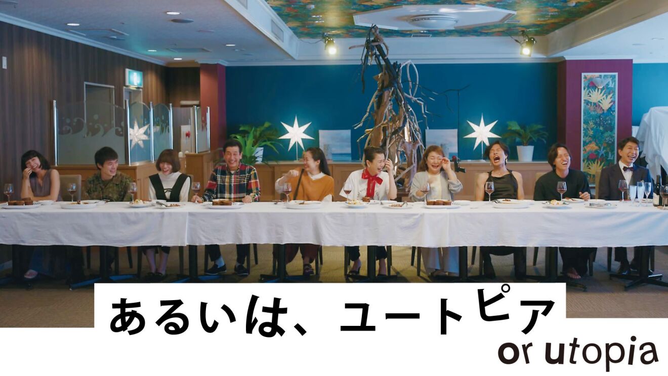不思議な飾りつけがされた部屋で、長いテーブルに一列になって女性6人と男性4人が笑いながら食事をしている