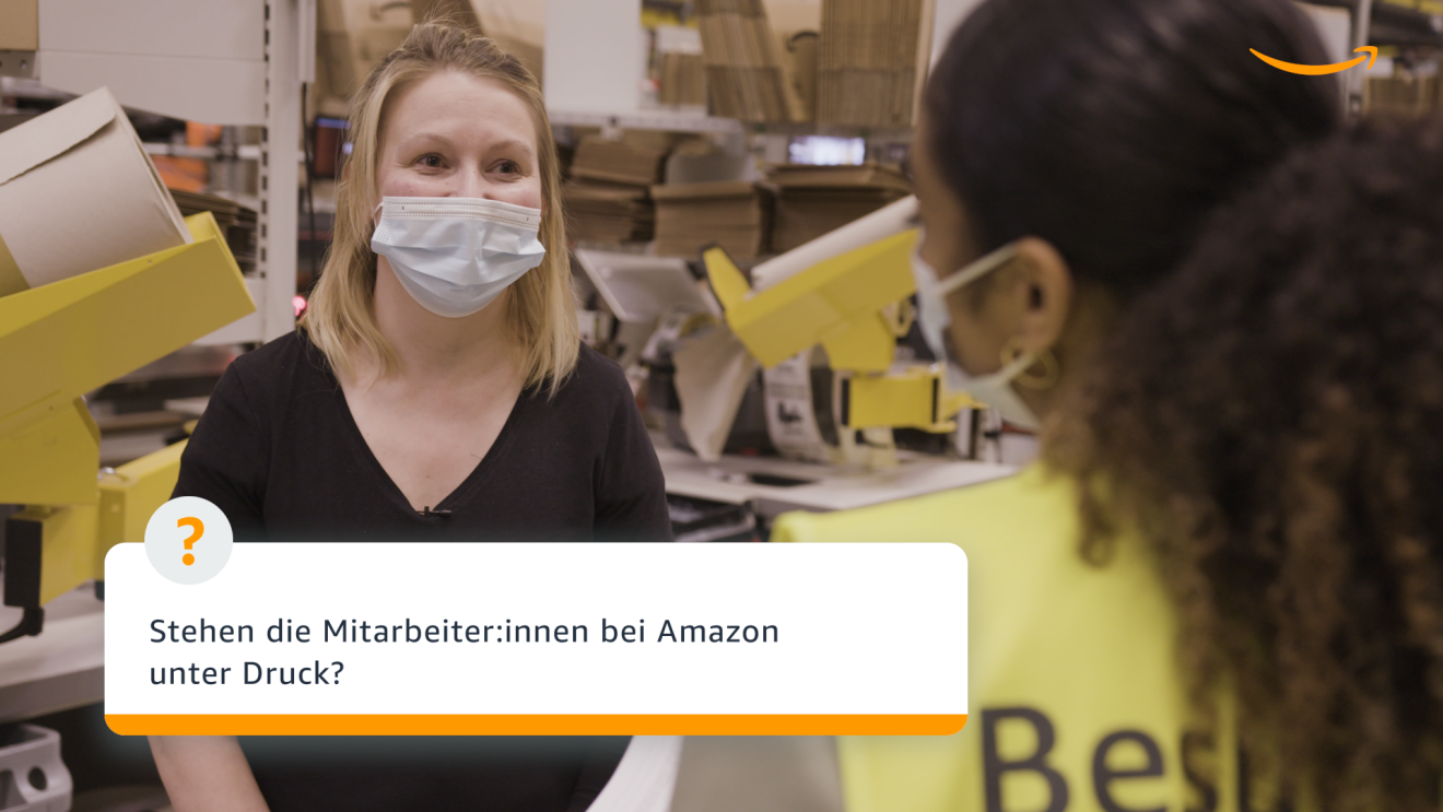 Eine Frau mit schwarzem Pulli und einer Maske schaut in die Kamera.