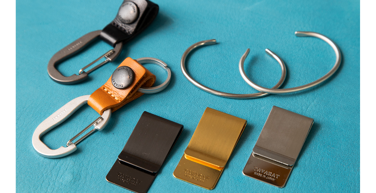 ブラックとキャメルのカラビナ式のキーホルダー、真鍮のバングル、ブラス・ブラック・シルバーのマネークリップなどの写真