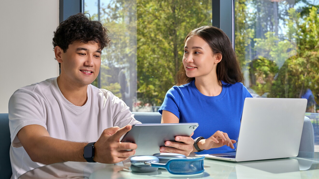 A man and woman sat in a modern office setting with a laptop and tablet