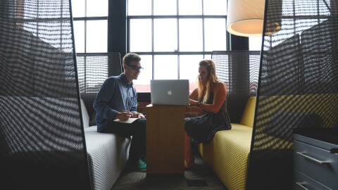 Man taking notes as his female colleague works on a laptop, in a casual work space.