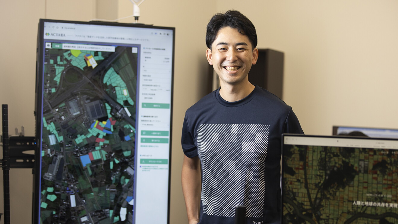 モニターの前に立つTシャツを着た男性