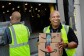 A smiling man holds boxes while people in the background load a truck. 