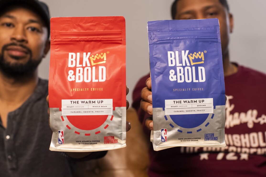 Two men hold bags of coffee labeled "BLK & Bold" and bearing the NBA logo.