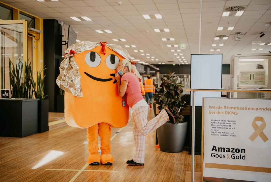 Eine Amazon Mitarbeiterin gibt dem Maskottchen Peccy einen Kuss.