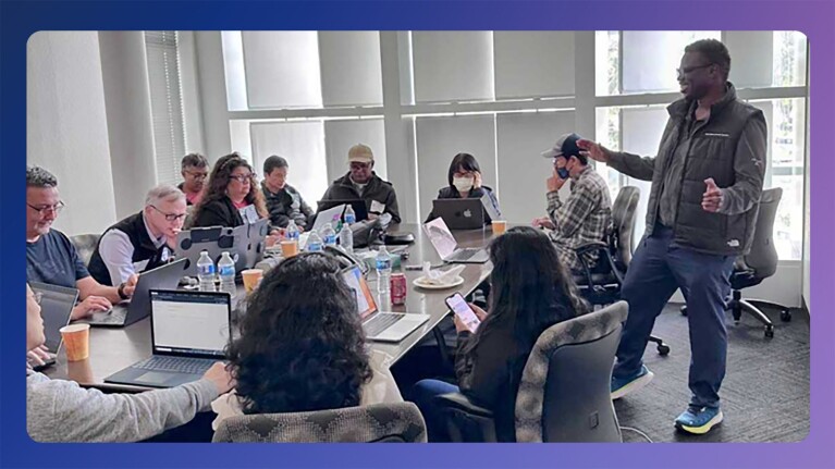 A photo of Banjo Obayomi, senior developer advocate, AWS, presenting at a workshop. There are several participants sitting around a conference room with their laptops on the table.