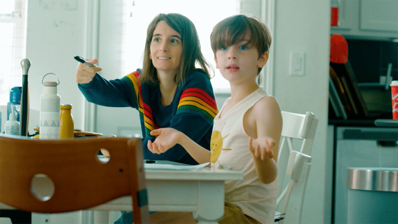 An image of a mom and her child looking across the room while sitting on the kitchen counter. The mom is pointing at something with a marker in her hand. 