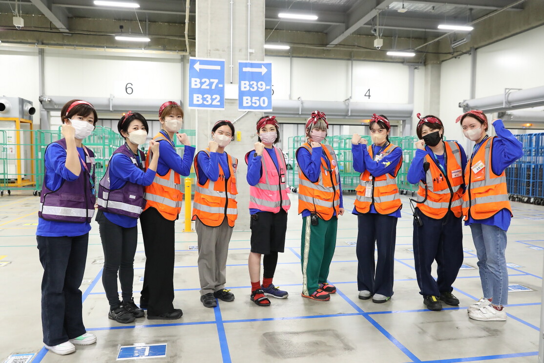 作業用のベストを着た9人の女性がガッツポーズをしている