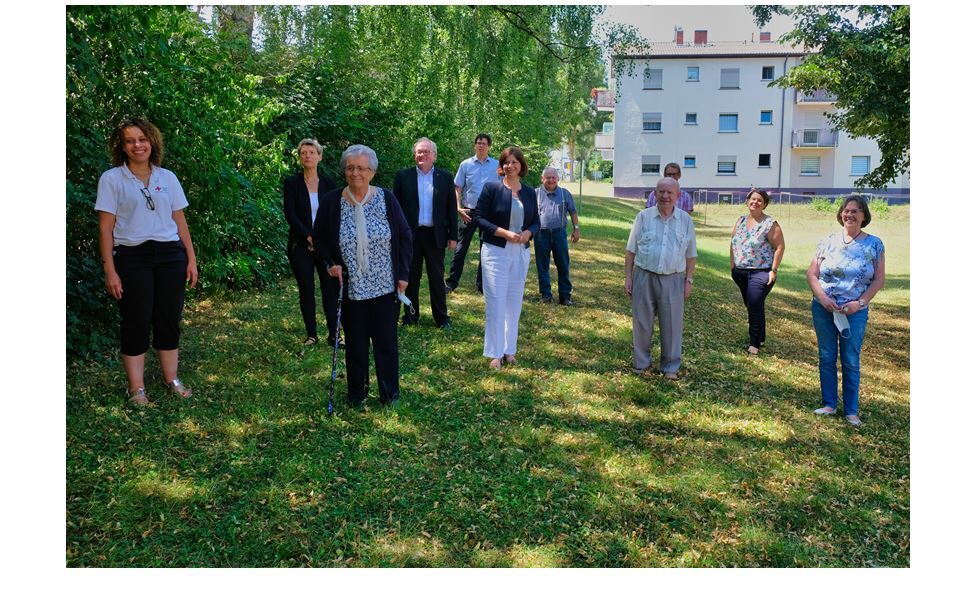 Auf einer grünen Wiese stehen Seniorinnen mit Abstand und lächeln in die Kamera. Die Sonne scheint.