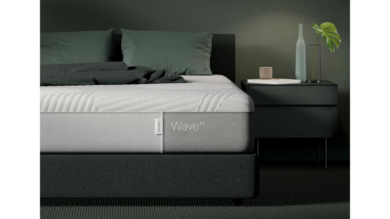 An image of a bed with a bare mattress on top. The mattress has the Casper logo on the end and text that says "Wave H."