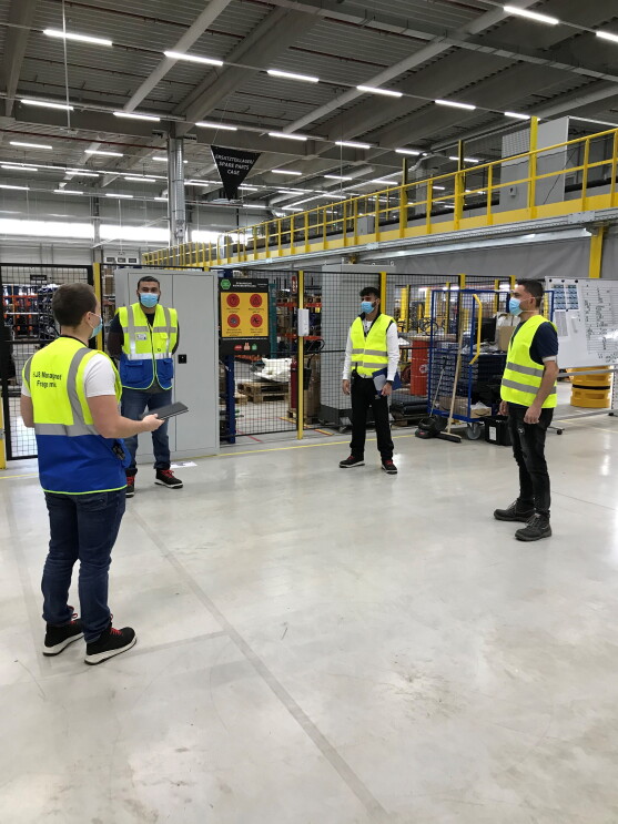 4 Mitarbeiter mit Sicherheitswesten und Masken in einer Logistikhalle