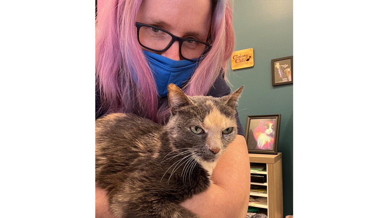 An image of a woman with pink hair taking a selfie with her cat in her veterinarian clinic. 