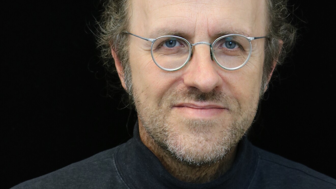 Bernhard Schölkopf, chief machine learning scientist for Amazon’s retail division, he wears a black turtle neck and wire framed silver glasses, and sits in front of a black background.