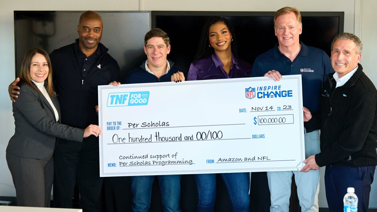 An image of multiple people from Thursday Night Football holding a large check made out to a charity.