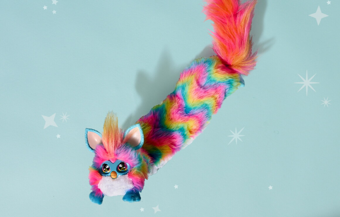 Colorful furby toy with long rainbow tail against starry blue background