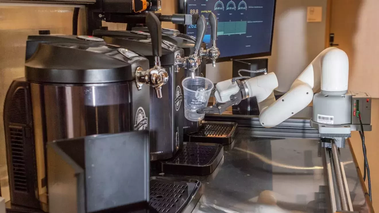 ロボットの手がプラスチックのコップを持って、3つ並んでいるコーヒーサーバーの下に置いている