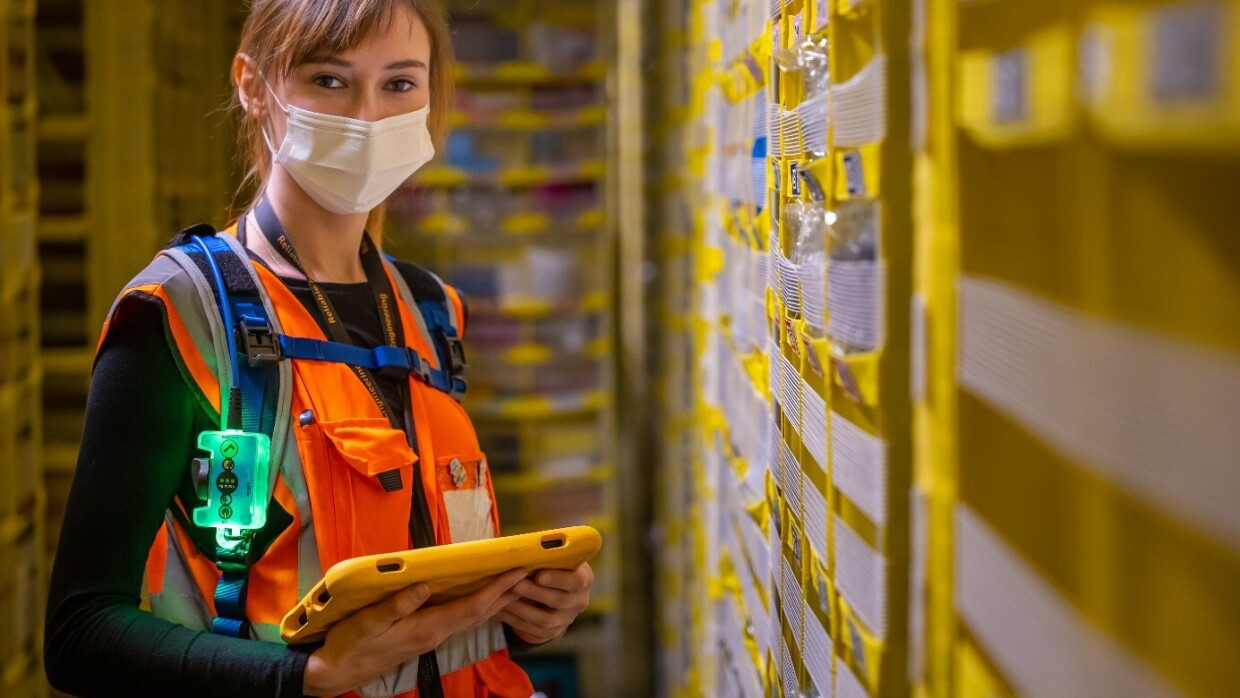 Arbeitsplatz in Gera. Mitarbeiterin, die eine orangene Weste und eine Maske trägt, mit Tablet in der Hand.