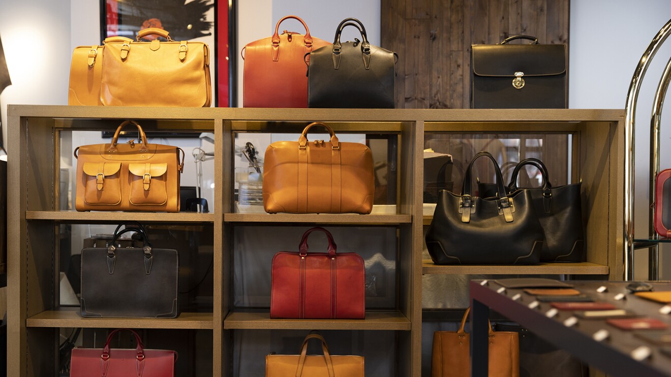 赤や黒、茶色などさまざまな色・大きさ・形の革製品の鞄が並べられている商品棚