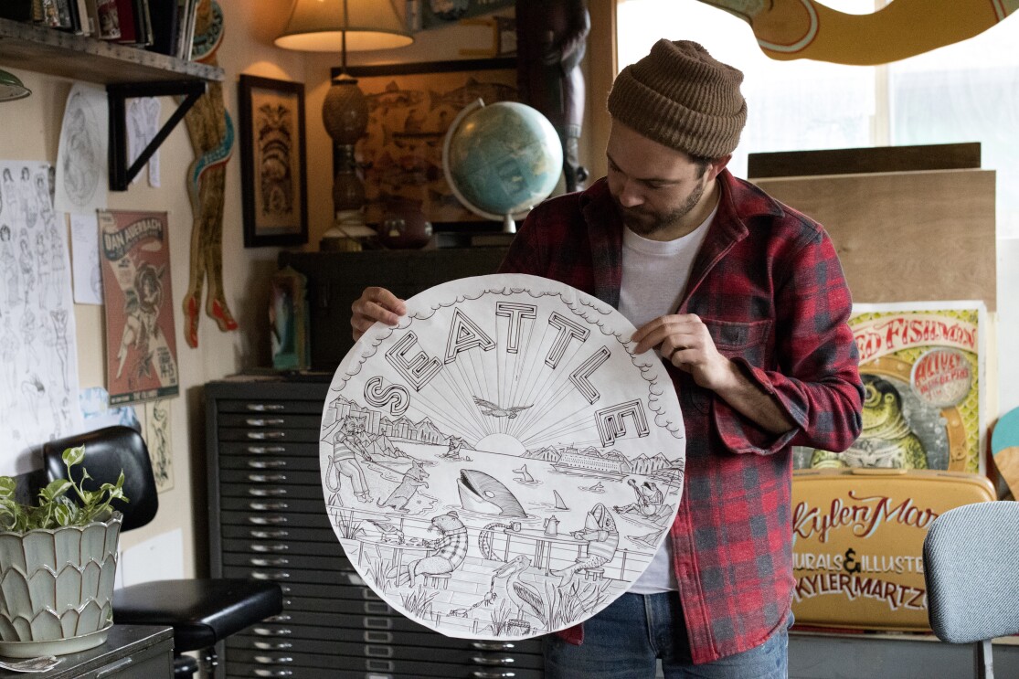 Kyler Martz in his Seattle studio , holding up a circular drawing labeled Seattle.