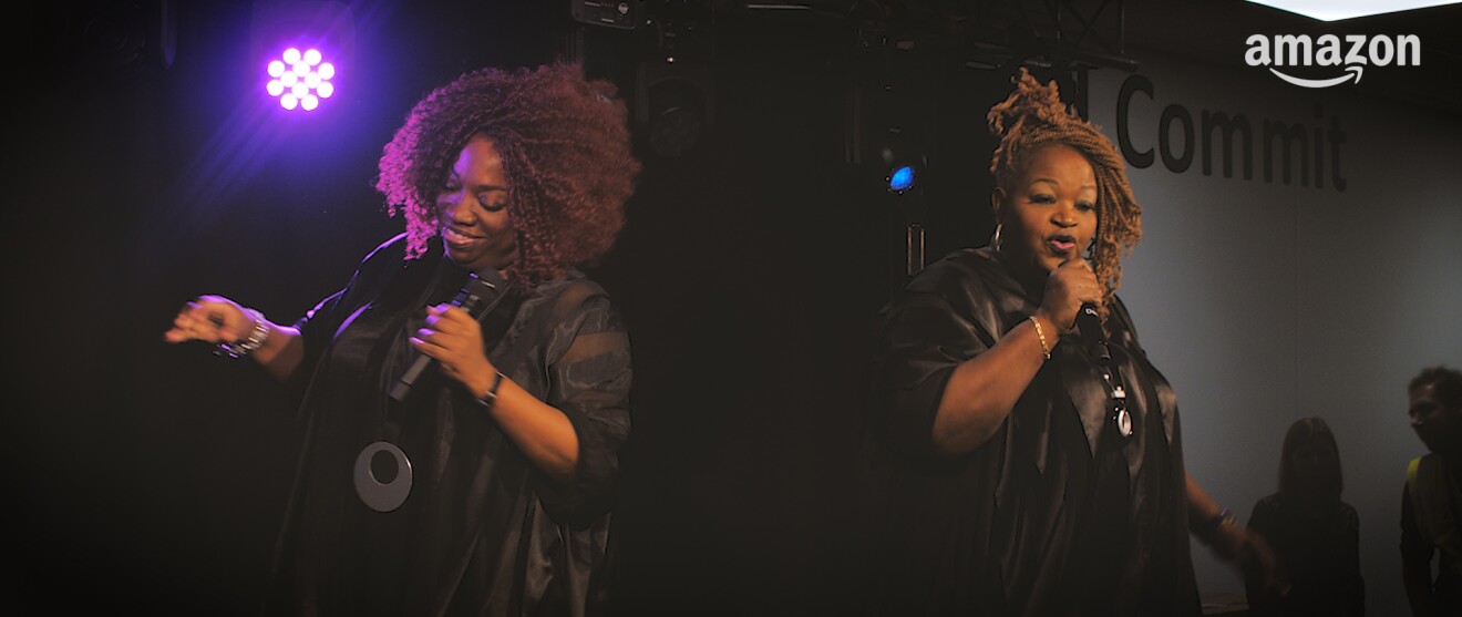 Zwei dunkelhäutige Sängerinnen stehen auf einer Bühne, in der Hand: Mikrofone