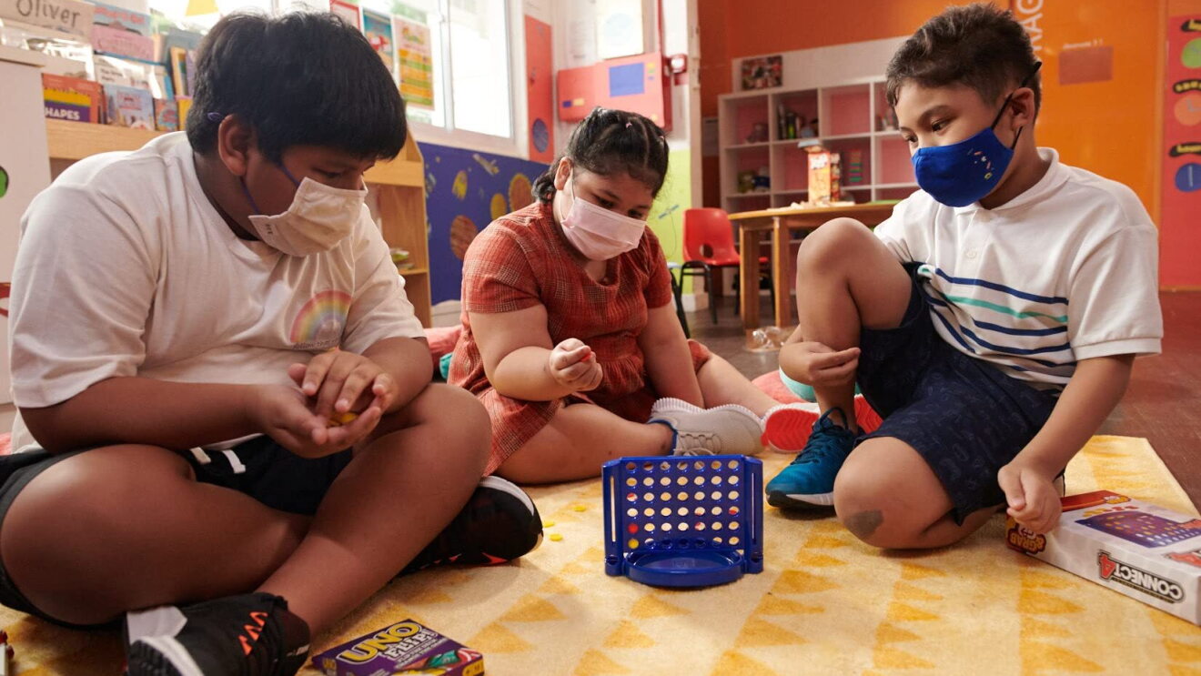 Children wear face masks and play with toys in a classroom-type setting
