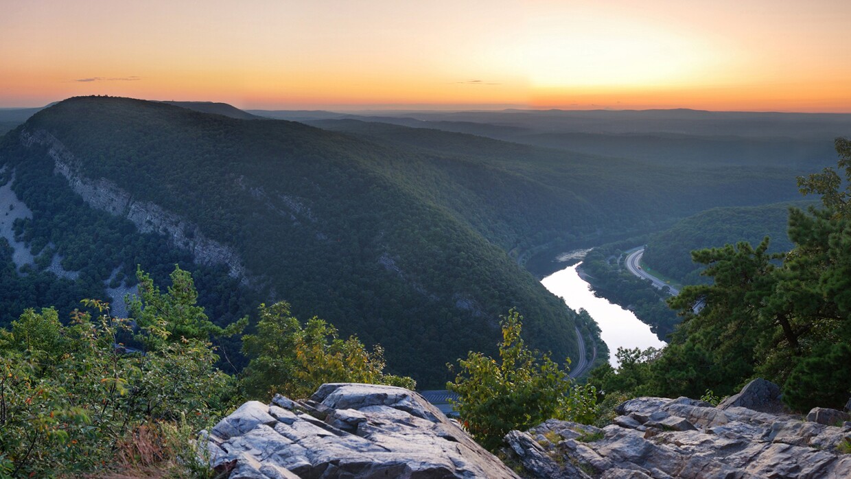 A view of the Appalacian mountains in Pennsylvania overlooking mountains, river, vegetation, in front of a sunset.