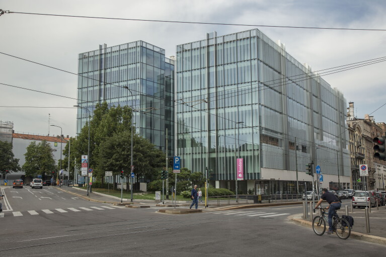 Due edifici in vetro visti dall'altro lato della strada. Gli edifici sono uguali e speculari. Un uomo in bicicletta a destra dell'immagine sta per attraversare la strada, mentre un pedone occupa l'incrocio. 