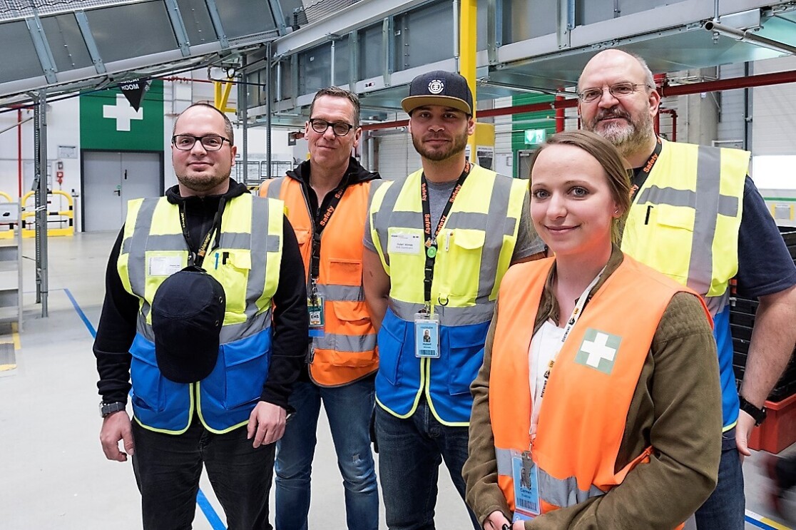 Vier männliche Mitarbeiter und eine Mitarbeiterin im Gruppenbild. Alle tragen Sicherheitswesten und lächeln in die Kamera